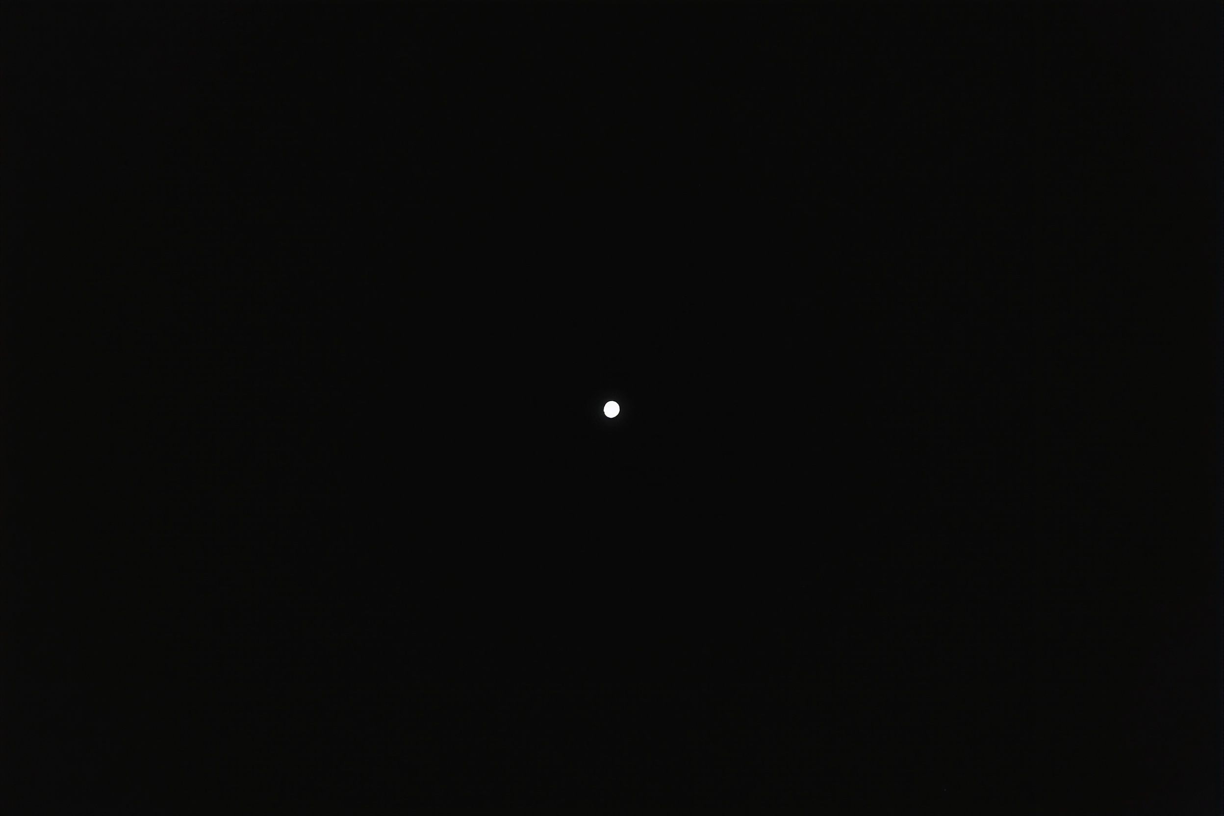 A single small white moon centered in a deep black sky, otherwise empty.